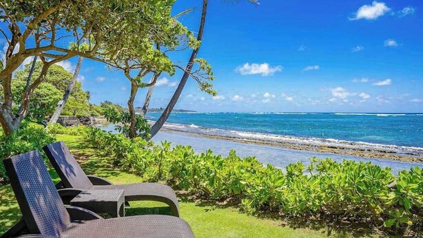 A beachside lounge area with chairs, a view of the ocean, and lush greenery. - *New* Kapaa Family Retreat with Two Pools and Lanai (Kapaa)
