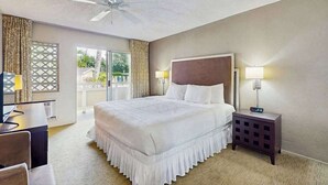A hotel room with a bed, bedside lamps, a desk, a chair, a ceiling fan, and a view through a window. - *New* Ground-Floor Kapaa 1BR Steps from the Beach (Kapaa)