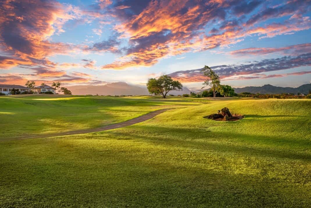 Un parcours de golf avec un chemin menant à un trou, entouré d’herbe et d’arbres, sous un ciel au coucher du soleil.