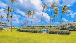 A well-maintained lawn, palm trees, a swimming pool, and a building in the background. - New Ground-Floor Poipu Escape Near Shipwreck Beach (Koloa)