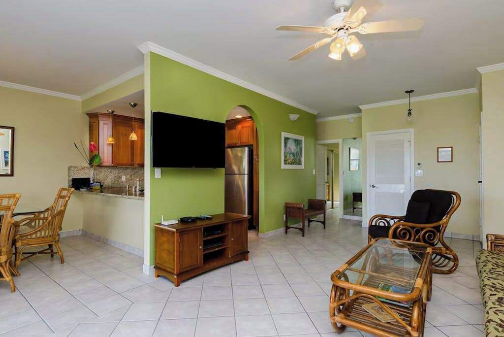 A living room with a TV, entertainment center, wicker furniture, and a ceiling fan.