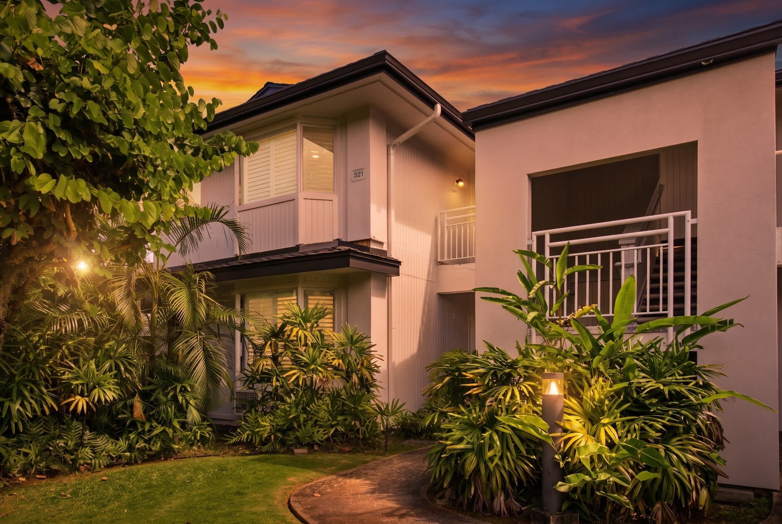 A two-story house with a balcony, surrounded by lush greenery and a well-maintained lawn.