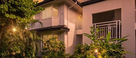 A two-story house with a balcony, surrounded by lush greenery and a well-maintained lawn.