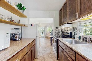 A kitchen with wooden cabinets, a granite countertop, a built-in oven, and a window with a view. - *NEW* Kauaʻi Ocean-View Studio With Lanai, Beach and Pool (Kapaa)