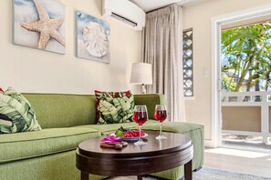 A green sofa with a tropical print pillow, a round wooden table with two wine glasses and fruit, and a starfish decoration on the wall. - Ground-Floor Kapaa Retreat 250 Yards from the Beach (Kapaa)