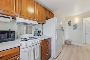 A kitchen with wooden cabinets, a stove, a microwave, and a refrigerator. - Ground-Floor Kapaa Retreat 250 Yards from the Beach (Kapaa)