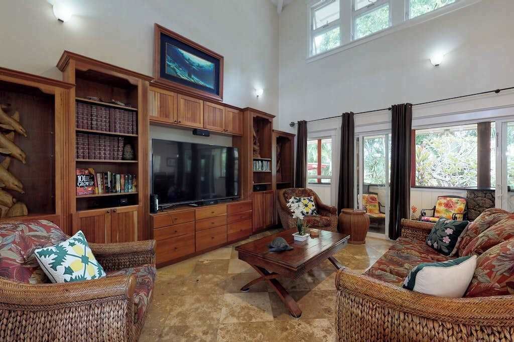 A spacious living room with a large flat-screen TV, wicker furniture, and a bookshelf.