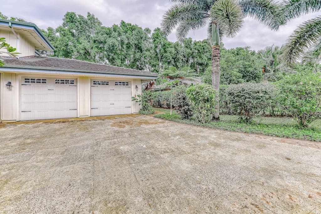 A two-story building with a garage, surrounded by lush greenery and palm trees.