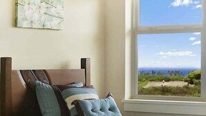 Une chambre à coucher avec un lit, des oreillers et une fenêtre donnant sur une plage et l’océan.