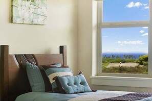 Ein Schlafzimmer mit einem Bett, Kissen und einem Fenster mit Blick auf Strand und Meer.