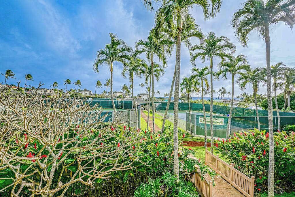 A tropical resort with palm trees, a wooden deck, and a tennis court.