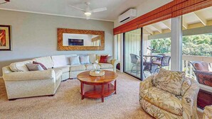 A living room with a sofa, a coffee table, and a patterned armchair. There is a ceiling fan, a large mirror, and a sliding glass door leading to an outdoor area. - *NEW* Air-Conditioned Poipu Retreat, 100 Yards from Brennecke's (Koloa)