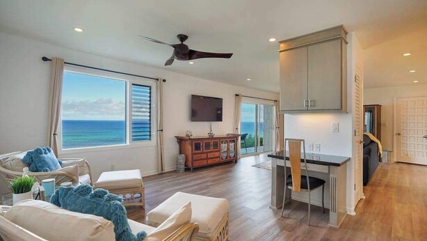 A spacious living area with a view of the ocean, a ceiling fan, a dining area, and a TV mounted on the wall. - *NEW* Princeville Ocean Views for Slow Kauai Mornings (Princeville)