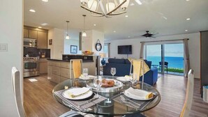 A modern dining area with a glass table, overhead lighting, and a view of the ocean. - *NEW* Princeville Ocean Views for Slow Kauai Mornings (Princeville)