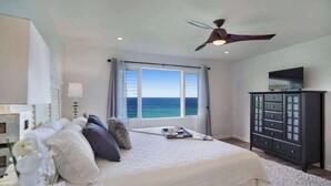 A bedroom with a large bed, a ceiling fan, a TV on a cabinet, and a view of the ocean. - *NEW* Princeville Ocean Views for Slow Kauai Mornings (Princeville)
