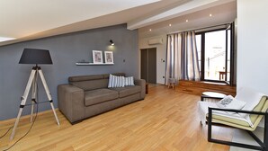 Ein modernes Wohnzimmer mit einer Couch, einem kleinen Tisch, einer Stehlampe und einem großen Fenster mit Vorhängen.