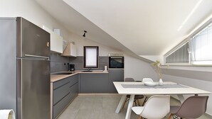 Eine moderne Küche mit Backofen, einem Esstisch mit Stühlen und einem Fenster mit Jalousien.