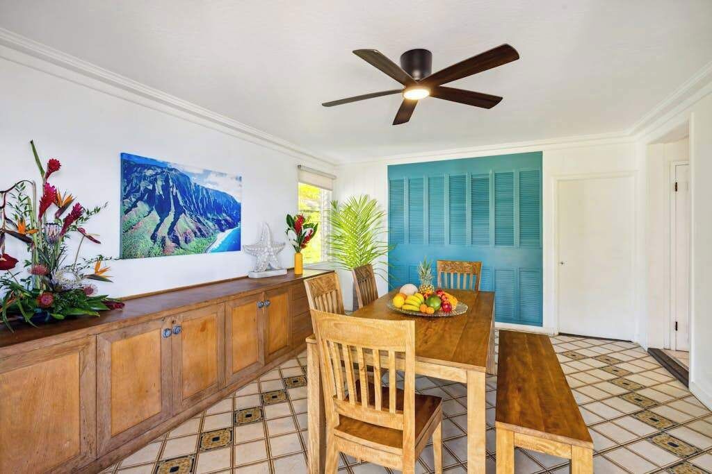 A dining area with a wooden table, chairs, a ceiling fan, and a wall-mounted painting.