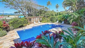 A swimming pool with lounge chairs, surrounded by tropical plants and palm trees. - *NEW* Beachfront Kapa'a Stay with Pool and Coastal Views (Kapaa)