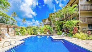 Una piscina con sillas de descanso, rodeada de plantas tropicales y un edificio de varios pisos.