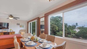 Un coin repas avec une table dressée pour quatre personnes, de grandes fenêtres et un ventilateur de plafond.