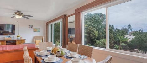 A dining area with a table set for four, large windows, and a ceiling fan.