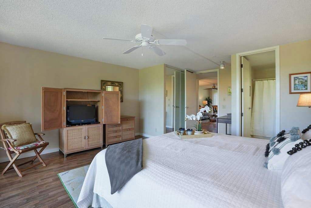 Habitación de hotel con cama, televisor, ventilador de techo, silla y baño visible a través de una puerta abierta.