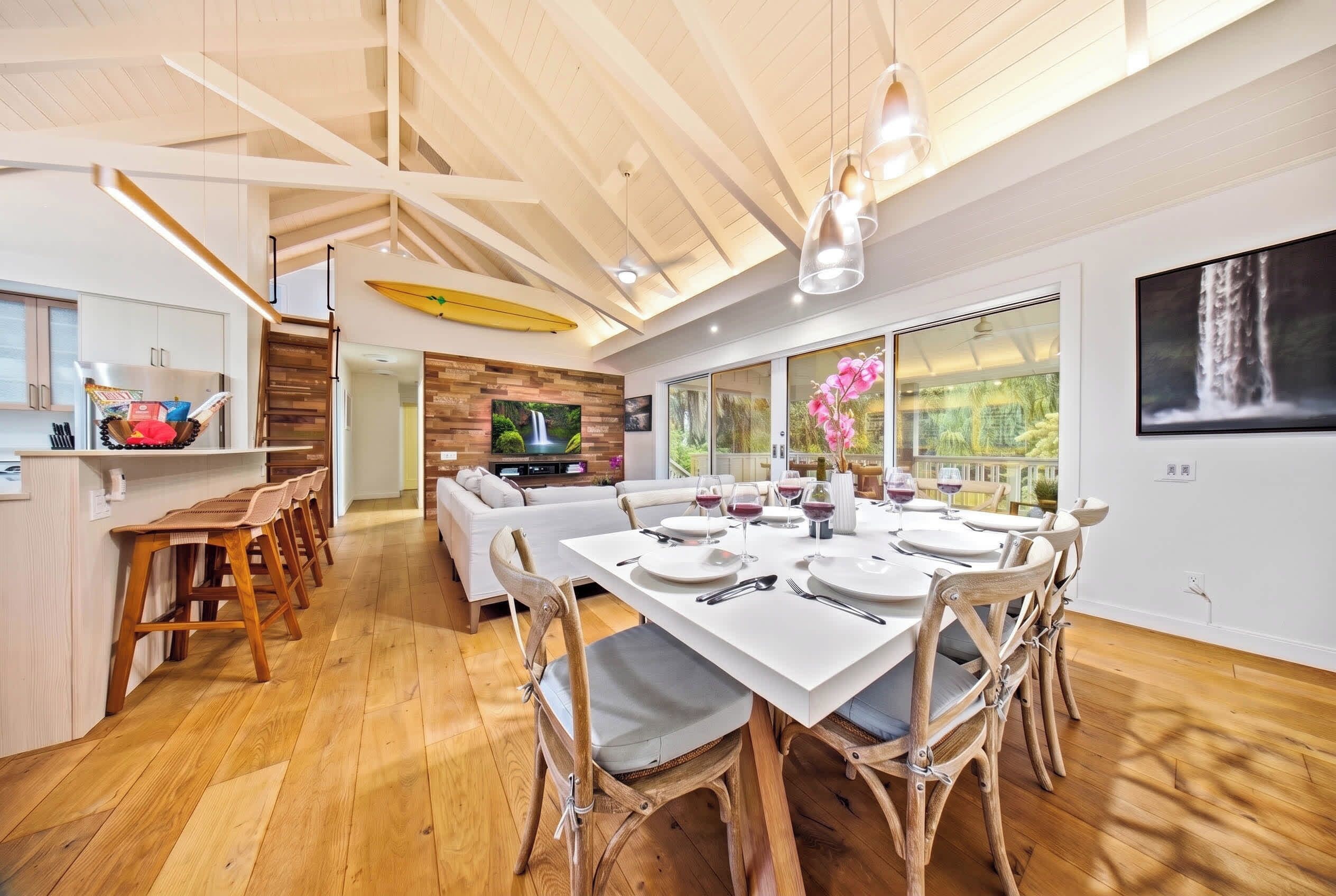 Une salle à manger spacieuse avec un plafond haut, un plancher en bois et une cuisine moderne en arrière-plan.