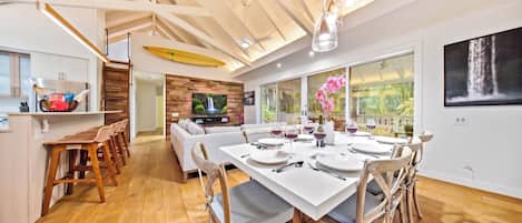 Une salle à manger spacieuse avec un plafond haut, un plancher en bois et une cuisine moderne en arrière-plan.