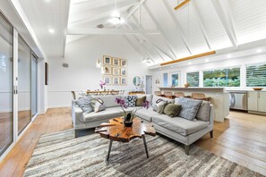 A spacious living room with a large sectional sofa, a coffee table, and a dining area with chairs. - Anini Beach Ke Hale Olu Family Retreat Cottage- Steps to Sand - Kitchen, WD, BBQ (Kilauea)