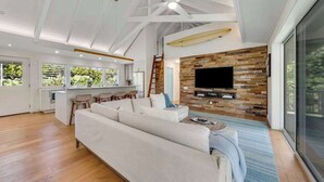 Un espacio habitable moderno con techos altos, un sofá grande, una unidad mural para televisión y una tabla de surf.