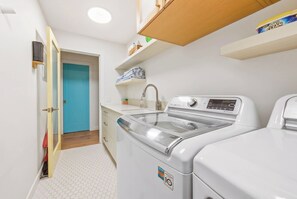 Ein Waschraum mit Waschmaschine und Trockner, einem Waschbecken und einer blauen Tür.