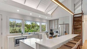 Una cocina moderna con una isla grande, armarios blancos y vista a la vegetación exterior.
