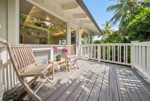 Une terrasse en bois avec deux chaises et une petite table, entourée d’une balustrade blanche et d’une végétation luxuriante.