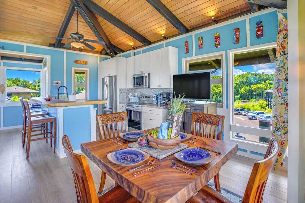 A kitchen with white cabinets, a microwave, and a TV. There is a dining table with blue plates and a pineapple centerpiece.