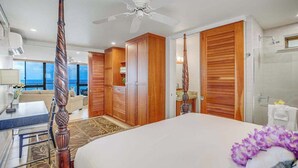 Hotelkamer met een bed, plafondventilator, houten kasten, een badkamer met douche en uitzicht op zee.
