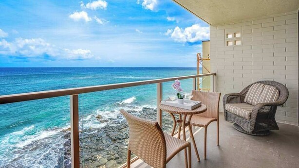 Een balkon met rieten meubels, een tafel met dienblad en uitzicht op de oceaan.