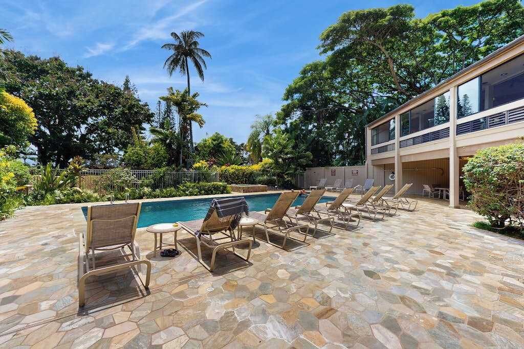 Un espace piscine doté de chaises longues, d’une terrasse carrelée en pierre et d’un bâtiment moderne avec de grandes fenêtres.