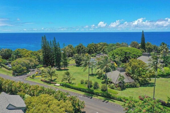 A residential area with a view of the ocean, houses with lawns, and a road. - Pali Ke Kua 209- Oceanview Oasis w/ AC, Pool, Hot Tub, Laundry, WIFI, Beach Fun (Princeville)