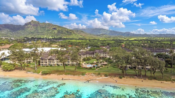 Ein Resort mit mehreren Gebäuden, einem Strand und klarem türkisblauem Wasser.