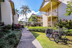 A pathway leading to a building with a balcony, surrounded by tropical plants and palm trees. - *NEW* Top-Floor Kapaa Studio with Partial Ocean and Garden Views (Kapaa)