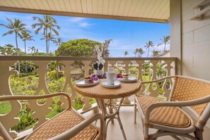 Un balcon avec des fauteuils en osier et une table où sont disposés une théière, des tasses et une assiette remplie de nourriture.