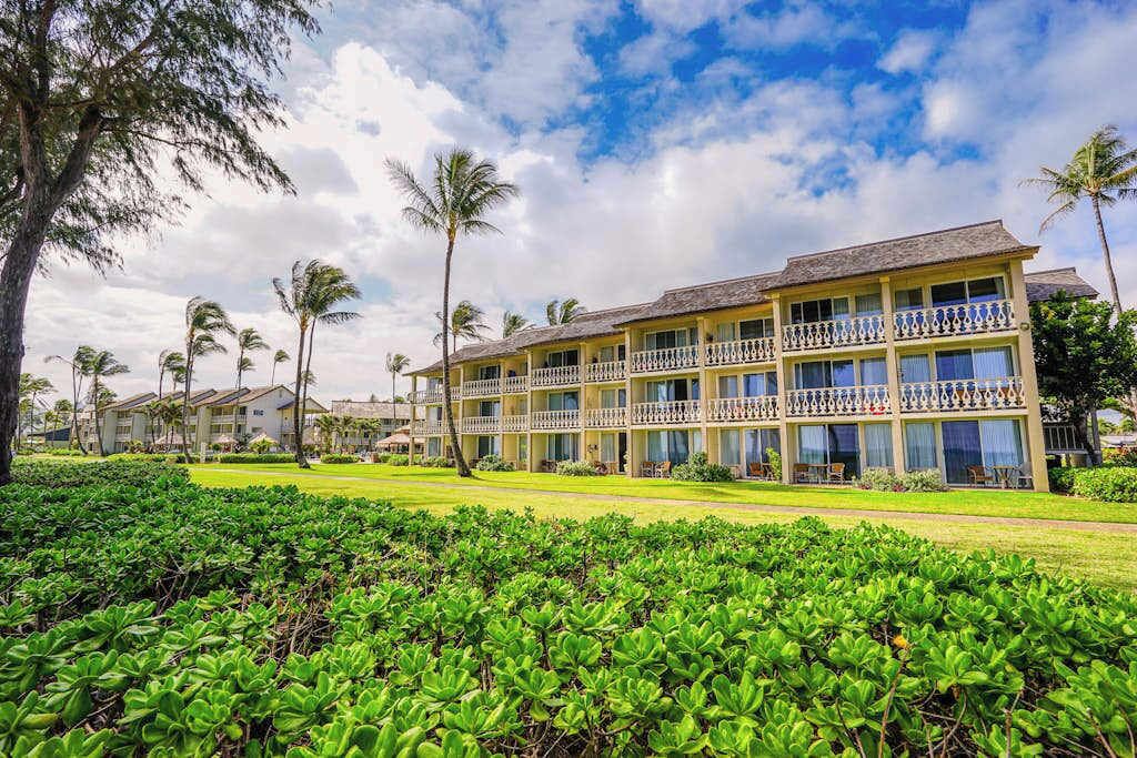 A multi-story hotel with balconies, surrounded by lush greenery and palm trees.