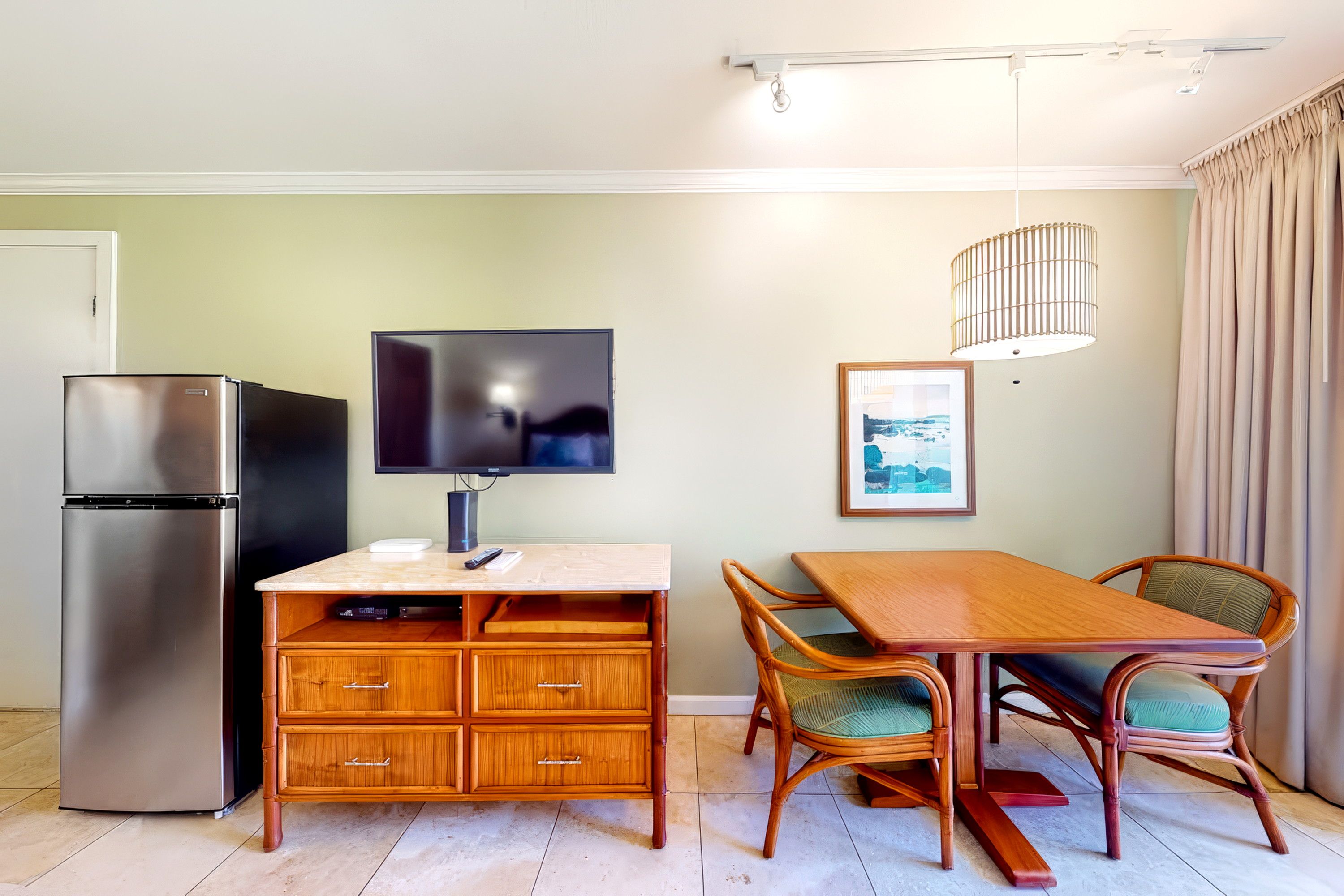 A compact living space with a kitchenette, a dining area with a wooden table and chairs, a television, and a framed picture on the wall.