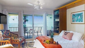 Een slaapkamer met een bed, een stoel, een tafel, een boekenkast en uitzicht op de oceaan.