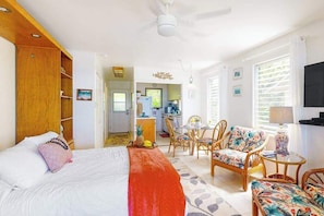 A hotel room with a bed, a dining area with chairs, a kitchen in the background, and a ceiling fan. - *NEW* Upper-Floor Kauaʻi Studio With Oceanfront Lanai (Kapaa)