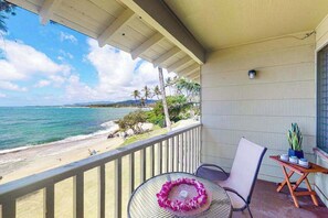 A balcony with a view of the beach and ocean, a table with a chair, and a small plant on a wooden table. - *NEW* Upper-Floor Kauaʻi Studio With Oceanfront Lanai (Kapaa)