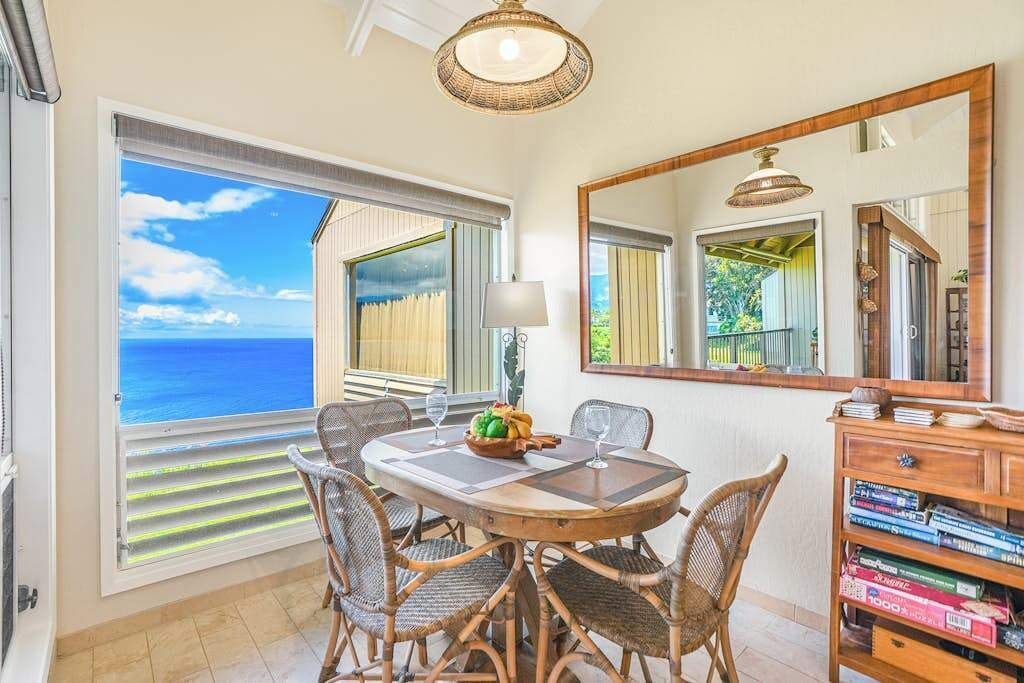 A dining area with a view of the ocean, wicker chairs, a round table, and a bookshelf.