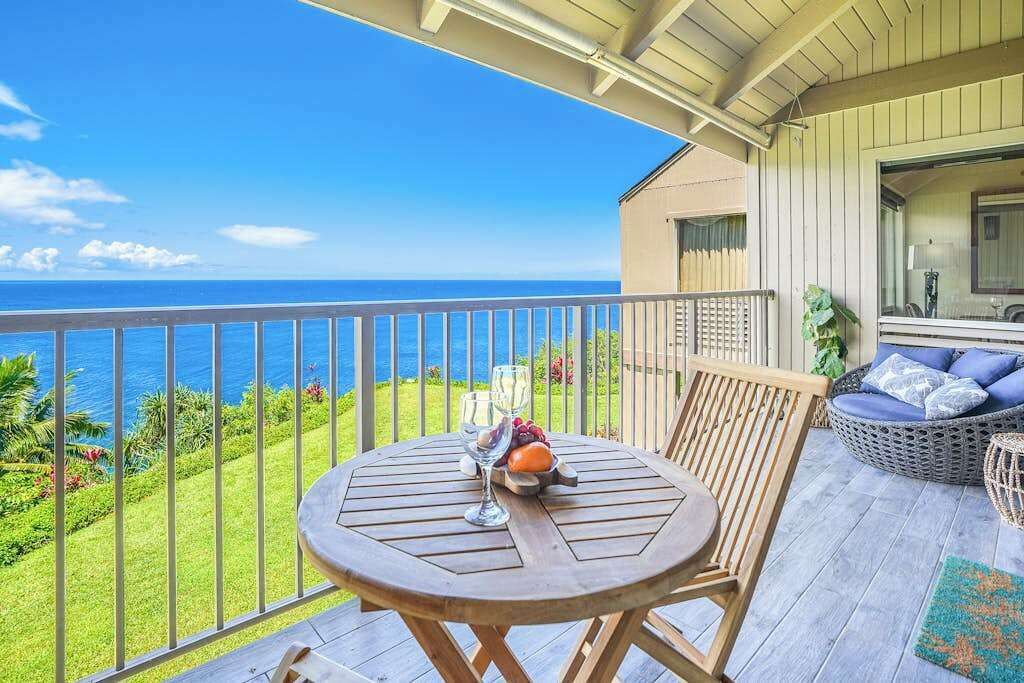 En träveranda med ett runt bord, en soffa av rotting och utsikt över havet.