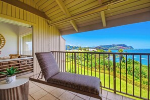 Ein Balkon mit einem Korbstuhl, einem kleinen Tisch mit einer Pflanze und Blick auf eine Küstenlandschaft.
